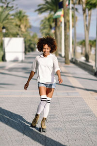 Portrait of smiling woman roller skating on footpath in city