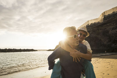 Man carrying woman while walking at beach against sky