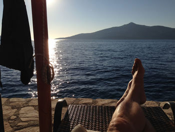 Low section of man relaxing on deck chair by sea against sky