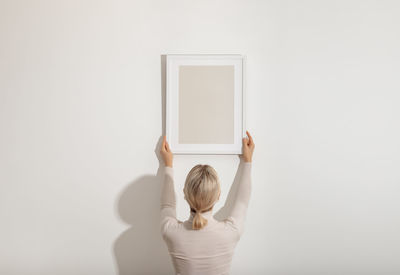 Rear view of woman holding picture frame against white background
