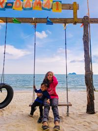 Portrait of siblings on swing at beach against sky