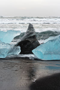 Ice blocks in blue and dark shades on a black beach with strong surf