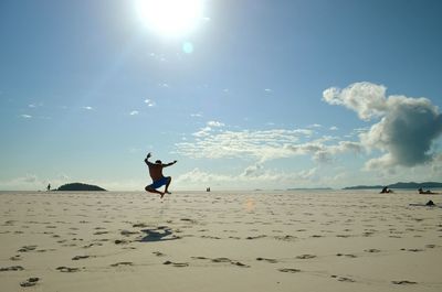 Rear view of shirtless man jumping at beach against sky
