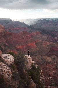 Man on rock by mountain against sky