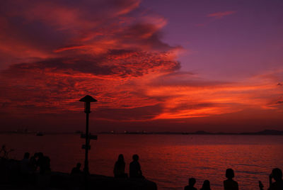 Silhouette people at beach against orange sky