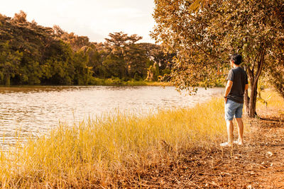 Rear view of man standing by lake against trees