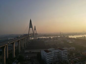 Suspension bridge in city against sky during sunset