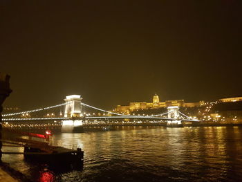 Illuminated bridge over river with city in background