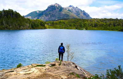 Rear view of man standing by lake against mountain