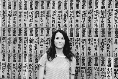 Portrait of smiling young woman standing against wall