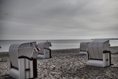 Hooded chairs at beach against sky