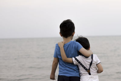 Rear view of boys standing at sea against sky