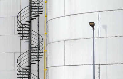 Low angle view of industrial staircase and streetlight against gas silo