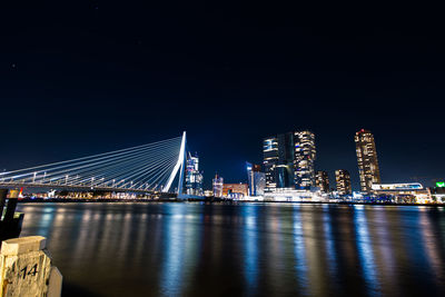 Illuminated bridge over river against buildings at night