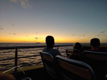 Silhouette people sitting by sea against sky during sunset