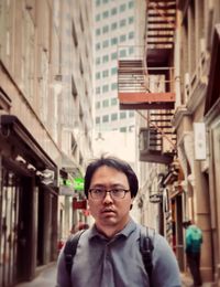 Portrait of young asian man standing against buildings in laneway in the city.