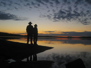 Silhouette couple standing on jetty against sea at sunset