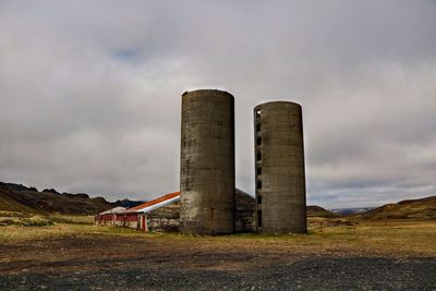 Factory on field against cloudy sky