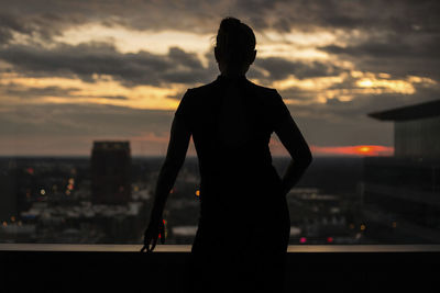 Rear view of woman standing on building terrace against city during sunset