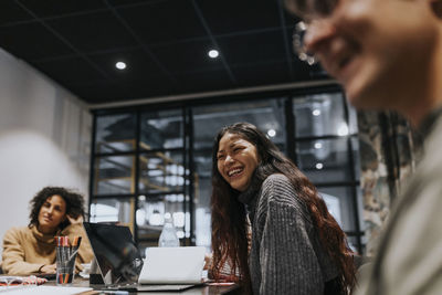 Young businesswoman laughing while discussing with colleagues during meeting in board room