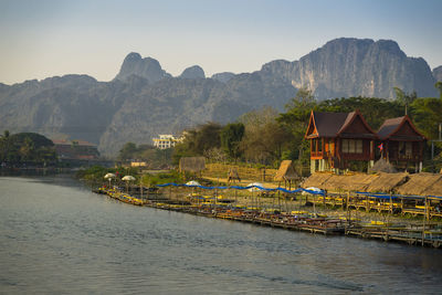 Houses by river and mountains against sky