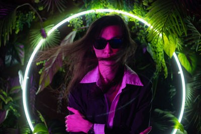 Portrait of young woman wearing sunglasses standing against plants