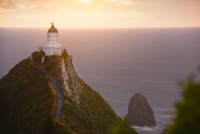 Lighthouse by sea against sky during sunset