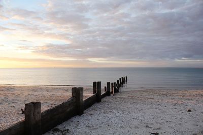 Wooden posts on sea against sky during sunset