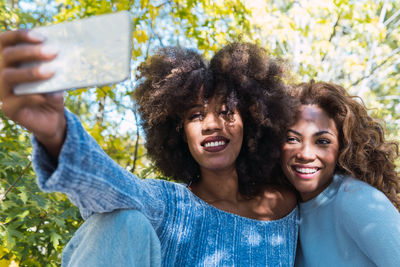 Close up of two female afro american friends with blue jumper smiling while taking selfie