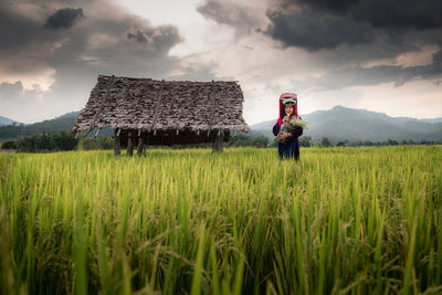 Woman standing at farm against cloudy sky