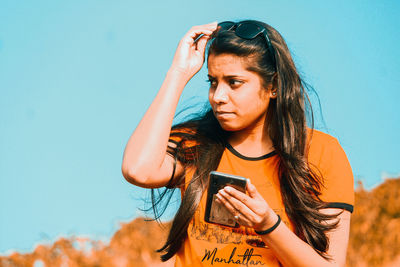 Young woman using mobile phone against blue sky