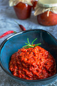 A bowl of homemade lutenica and jars of the same on a gray background