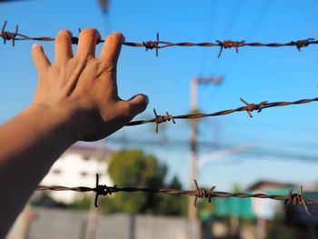 Close-up of hand holding barbed wire against sky