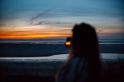 Rear view of woman standing at beach against sky during sunset