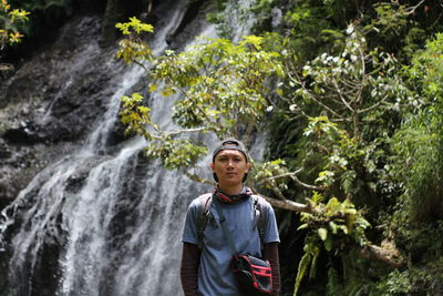 Young man standing by waterfall in forest