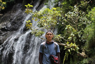Young man standing by waterfall in forest