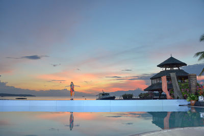 View of swimming pool by building against sky during sunset