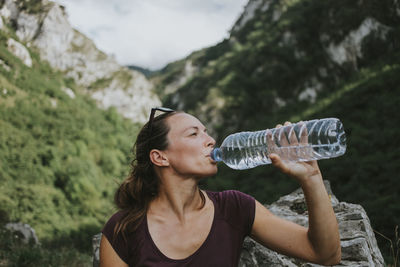 Mid adult female trekker drinking from plastic water bottle while looking away