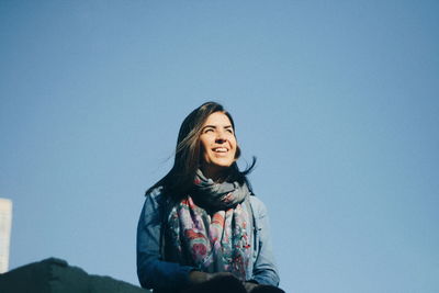 Smiling young woman sitting against clear blue sky
