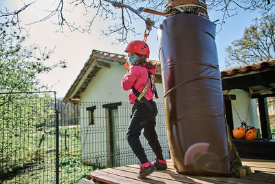 Little girl with protections practicing climbing between trees with ropes and nets