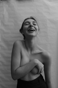 Shirtless woman standing against wall