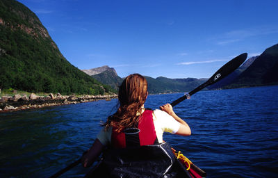 Rear view of woman kayaking in sea against sky