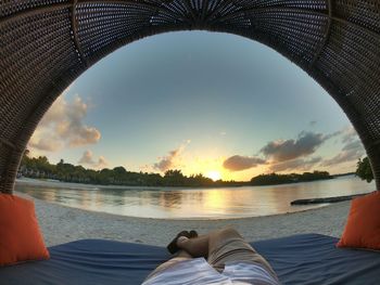 Low section of man relaxing on shore during sunset