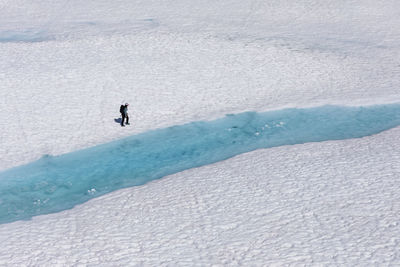 Drone view of unrecognizable female hiker walking along melting lake with clear blue water during vacation in british columbia