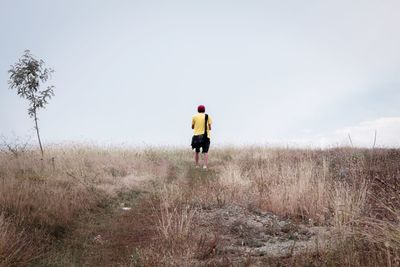 Rear view of man standing on field against sky