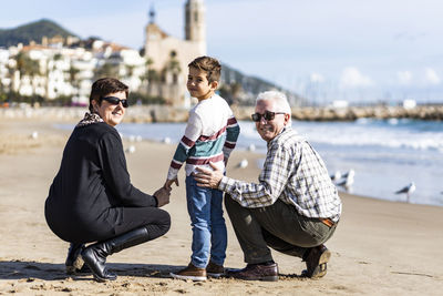 Portrait of happy grandparents with grandson crouching at beach