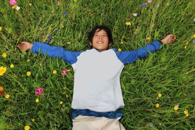 High angle view of teenage girl with arms outstretched lying on grassy field