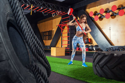 Young athletic woman hitting a hammer on an automobile tire in the gym. 
