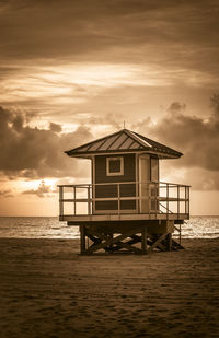 Built structure on beach by sea against sky during sunset