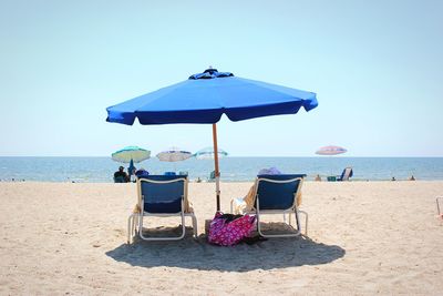 Deck chairs on beach against clear sky during sunny day